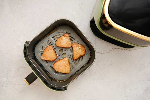 Juicy tuna steaks in a basket of an air fryer, where they are being cooked. The countertop features