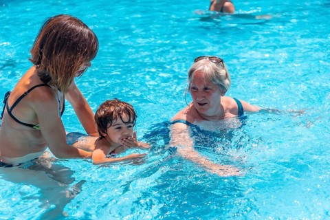 Mother and grandmother having fun with grandson in pool on summer vacation, learning to swim