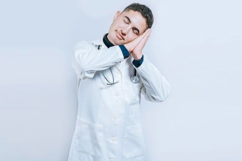 Young doctor making sleep gesture isolated. Handsome doctor making sleep gesture with palms on his
