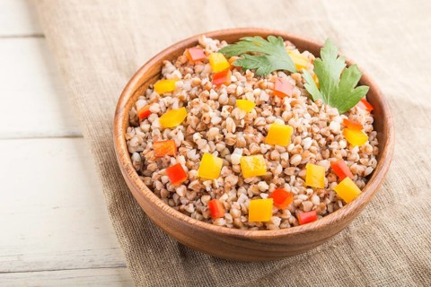 Buckwheat porridge with vegetables in wooden bowl on a white wooden background and linen textile.