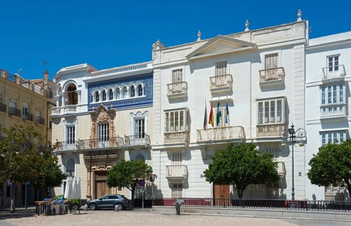 Historic buildings with white facade and trees on a square under a blue sky, left Casa Palacio