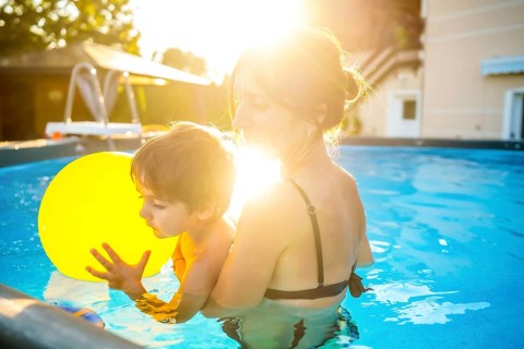 Mother and son enjoying summer vacation in a home swimming pool playing with a yellow inflatable
