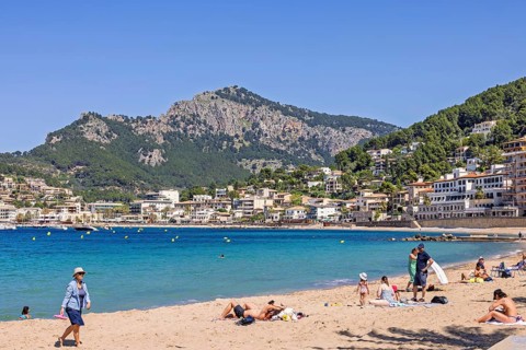 People sunbathing on the sand beach at a spanish coast village with houses at a sea bay, Port de