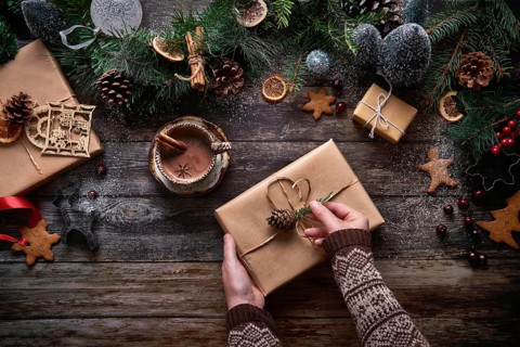 Top view of an anonymous woman preparing a Christmas present next to a bowl of chocolate and