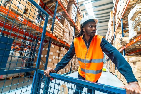 African male worker moving goods pushing a cart in a distribution warehouse