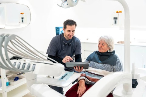 Dentist showing information on digital tablet to a senior patient during a consultation in a modern