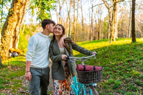 Romantic couple enjoying a leisurely stroll in a park with their bicycle, sharing a tender kiss