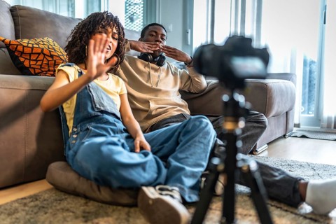 Two vloggers are sitting on cushions on the floor greeting their followers and recording a video