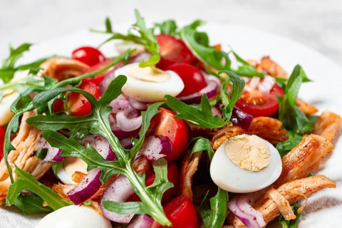 A warm salad with fried chicken fillet, arugula and cherry tomatoes, and boiled quail eggs, on a