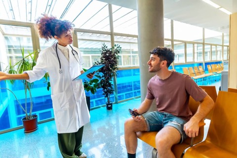 Doctor holding a clipboard, discussing diagnosis with a patient seated in a waiting area, fostering