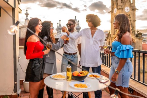 Multi-ethnic males and females friends eating snacks and beverages on a rooftop during sunset