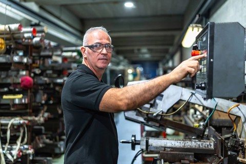 Mature caucasian man operating in the control panel of a mechanical saw in a metal cnc factory
