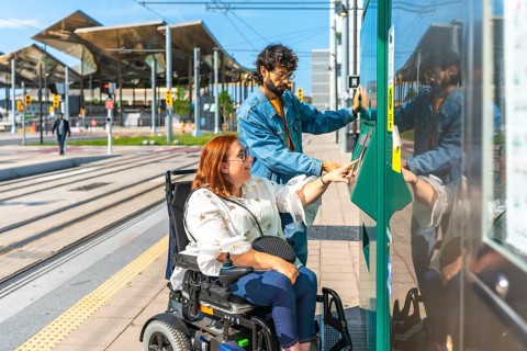 Young redhead woman sitting in a wheelchair and her friend buying a ticket at an automatic vending