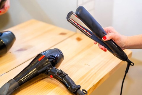 Close-up of a hairdresser hand grabbing a flat iron next to a hairdryer