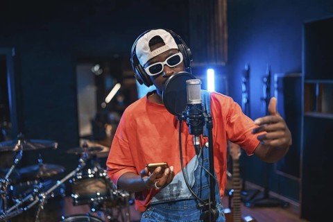 Young stylish male singer recording a new song in professional music studio, wearing headphones and