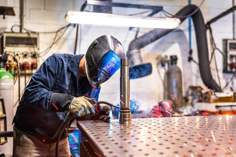 Three quarter length photo of a welder with facial mask and safety work wear working in factory