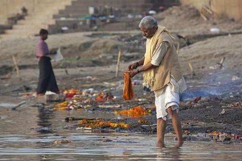 Indian man washing linen in polluted water of the Ganges river at Varanasi, Uttar Pradesh, India