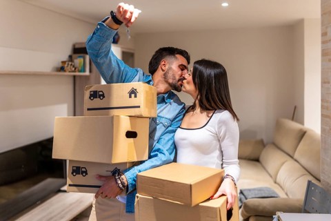 Young couple kissing while holding cardboard boxes and keys to their new apartment, celebrating