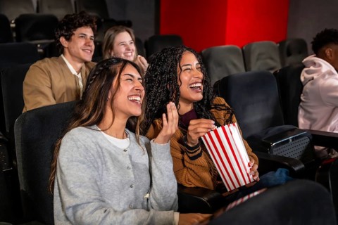 Friends enjoying a comedy film in a movie theater, laughing and sharing popcorn while soaking in