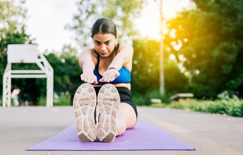 Athlete woman sitting doing leg stretch in a park. Athlete girl sitting on a mat stretching her