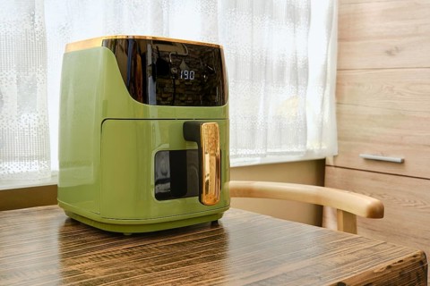 Preheating an air fryer on a wooden table in a well-lit kitchen. Sunlight streams through a