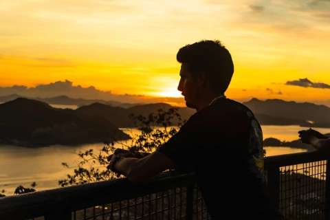 Silhouette of a tourist leaning on a railing, admiring the breathtaking golden sunset over coron