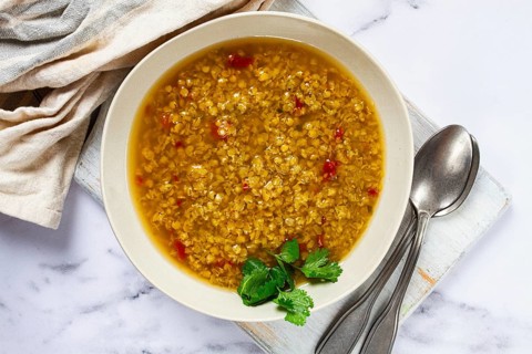 A steaming bowl of lentil soup fills the frame, showcasing a rich golden broth with pieces of red