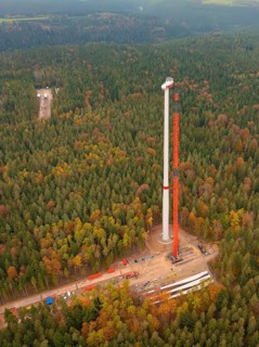 A wind turbine is erected with the help of a crane in the dense autumn forest, wind farm