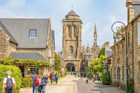 City street with tourists and the St Ronan's church steeple in the old town Locronan, Locronan,