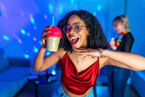 Cheerful young woman enjoying nightlife, holding a fancy beverage and dancing with friends in a