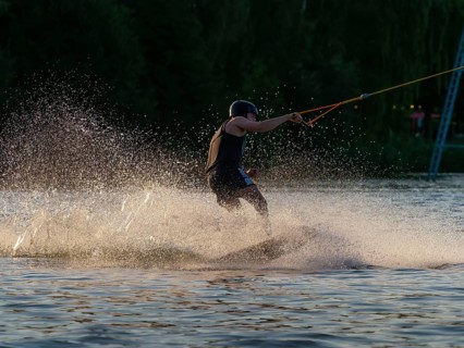 Man with wakeboard in splashing water, evening light, water sports and water skiing in wakepark