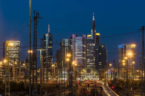 View over rails and moving train to the luminous main station, in the background the colourful