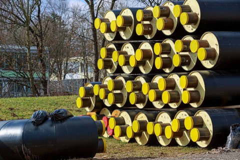 Stacked district heating pipes with yellow ends lie piled up in a meadow