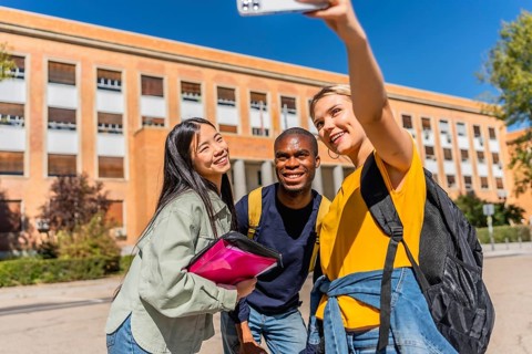 Happy multi-ethnic young university students taking selfie outside the university