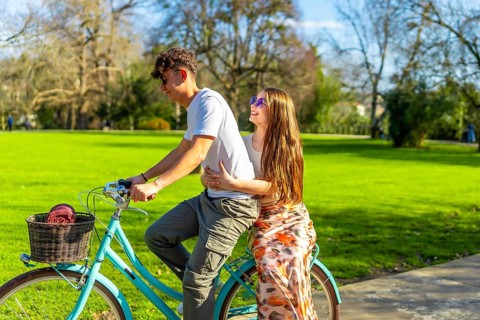 Teenagers riding a bicycle in a park, embracing and smiling, enjoying a sunny day together
