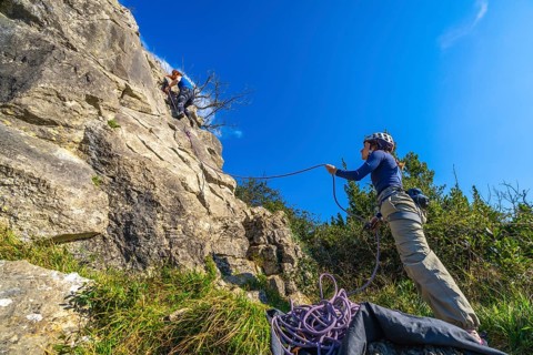 Two female climbers ascending a rock face, one belaying the other, ensuring safety during their