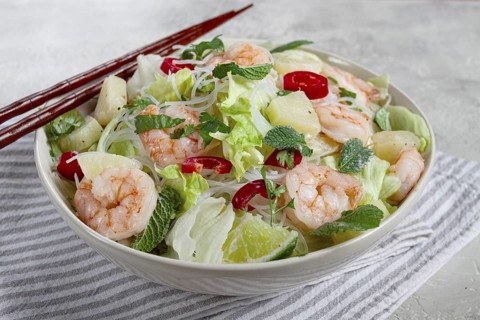 Thai salad with shrimp and rice noodles, pineapple slices, coriander and mint leaves, on a white