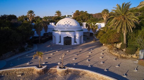 Drone shot, morning light, white dome on paved square, surrounded by palm trees in Mediterranean
