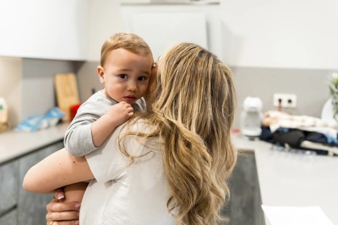 Mom holding her toddler in the kitchen, sharing a tender moment amidst daily chores, capturing the