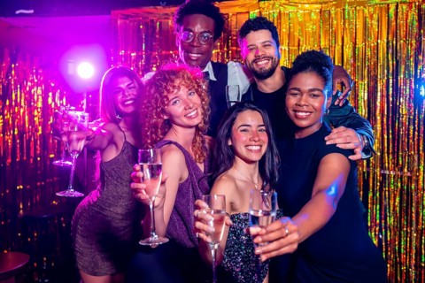 Group of cheerful elegant friends toasting champagne flutes, enjoying nightlife together at trendy