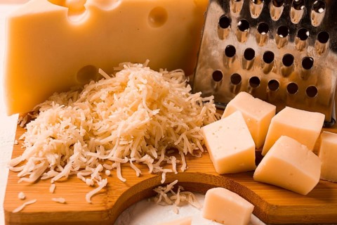 Geriebener Käse, Maasdam, auf einem Schneidebrett, Reibe und Käsemesser, Nahaufnahme, keine