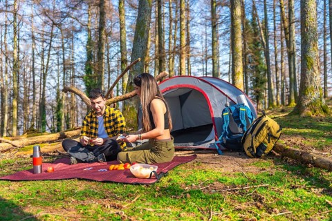 Hikers enjoying a card game and snacks in front of their tent during a camping trip in the woods