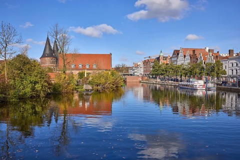River Trave, Holstentor, historic salt warehouse, trees, blue sky with fair weather clouds,