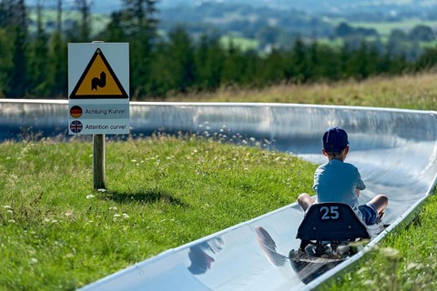 Boy with toboggan on the summer toboggan run, warning sign Attention curve, ski and toboggan arena,