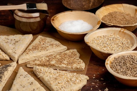 Triangles of dough, sprinkled with various grains and salt, on a rustic wooden table