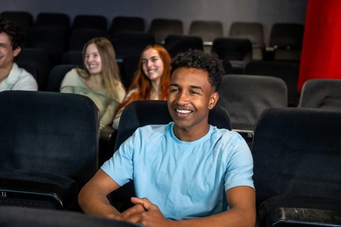 Young man smiles while watching a movie in a cinema, surrounded by his friends, enjoying a shared
