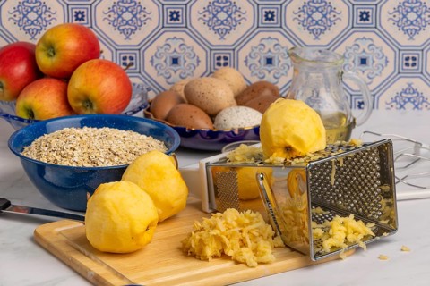 Grated and peeled apples on a chopping board, oat flakes and other ingredients behind them