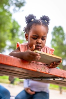 African little girl focus on the screen of a mobile in a park. Addiction concept