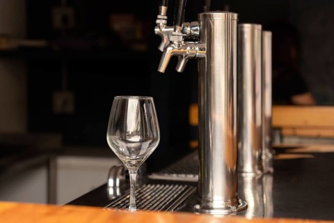 An empty glass cup next to a beer tap at the bar of a bar, ready for use. The set reflects a modern