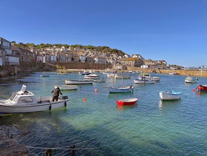 Scene in a busy harbour with people swimming and paddling in the water, Mousehole, Cornwall, Great